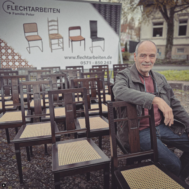 Mitarbeiter vor gestapelten Stühlen in der Flechtwerkstatt Familie Peter